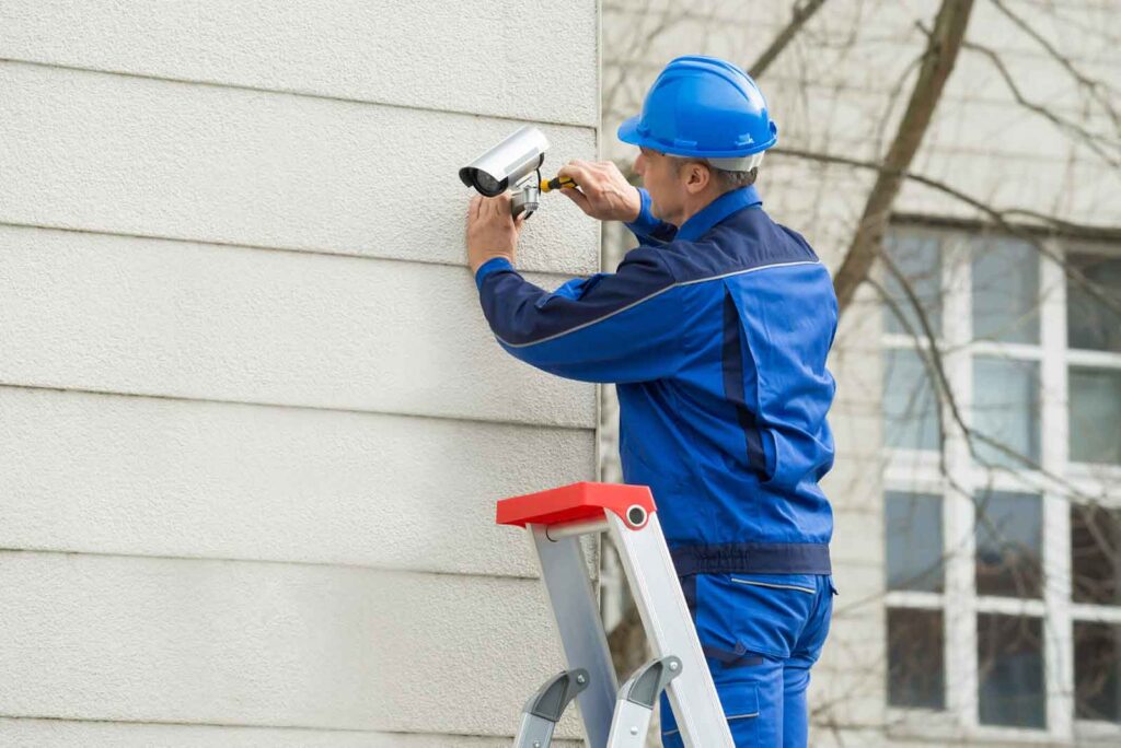 male technician standing on stepladder fitting cctv camera 1
